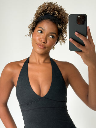 Woman taking a selfie with a black halter top dress on a plain background
